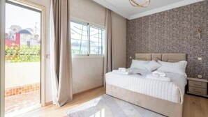 Un dormitorio con cama, mesita de noche, ventana con cortinas y vistas a edificios.