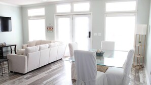 Un salon moderne avec un canapé blanc, une table à manger en verre et des chaises blanches.