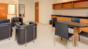 A modern hotel room with a dining area featuring a round table and chairs, a kitchen with wooden cabinets, and a seating area with sofas and a mirror. - Safari Lodge Hotel (Cisarua)