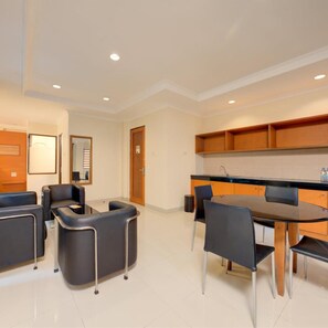 Une chambre d’hôtel moderne dotée d’un coin repas avec une table ronde et des chaises, d’une cuisine avec des meubles en bois et d’un coin salon avec des canapés et un miroir.