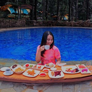A person seated at a table with various food items and a pool in the background. - Safari Lodge Hotel (Cisarua)