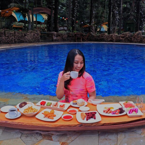Une personne assise à une table, devant divers plats, avec une piscine en arrière-plan.