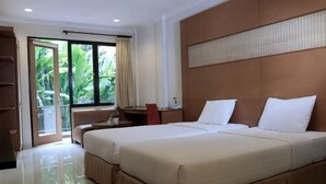 A hotel room with two beds, a desk, a chair, a wardrobe, and a sliding glass door to a balcony. - Safari Resort (Cisarua)