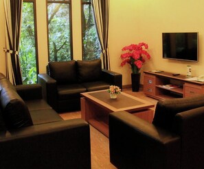 A living room with a sofa set, a coffee table, a TV, and a desk with a chair. - Safari Lodge Hotel (Cisarua)