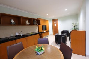 A modern kitchen with wooden cabinets, a dining table with chairs, and a small TV on the counter. - Safari Lodge Hotel (Cisarua)