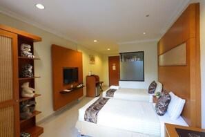 A hotel room with two beds, a TV, a desk, and a shelf with stuffed animals. - Safari Lodge Hotel (Cisarua)