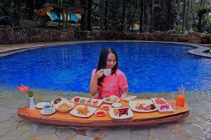 A person seated at a table with a variety of food and drinks by a pool. - Safari Lodge Hotel (Cisarua)