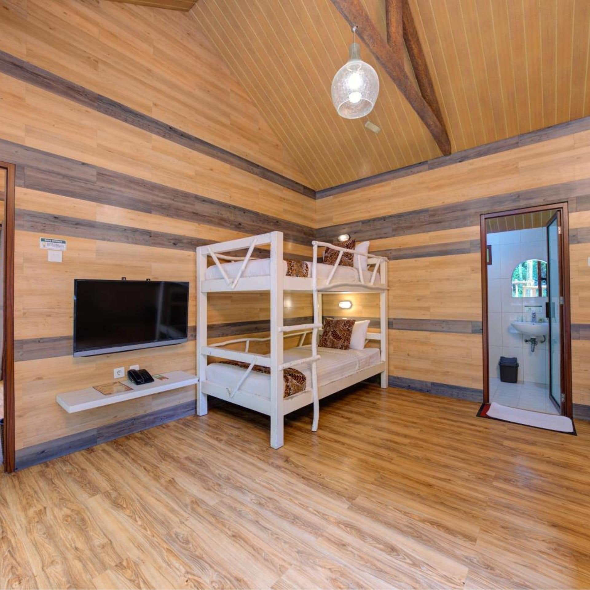 A room with a bunk bed, a flat-screen TV, and a wooden floor.