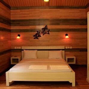 A bedroom with a wooden headboard, a bed with white linens, two bedside tables, and wall-mounted lamps. - Safari Lodge Hotel (Cisarua)