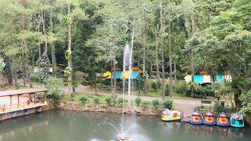 A tranquil pond with a central fountain, surrounded by lush greenery and colorful buildings.