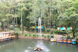 A tranquil pond with a central fountain, surrounded by lush greenery and colorful buildings. - Safari Lodge Hotel (Cisarua)