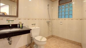 A bathroom with a sink, toilet, shower, and a window with blue-tinted glass. - Safari Lodge Hotel (Cisarua)