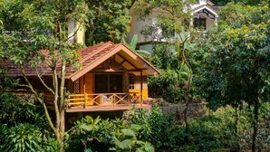 A wooden cabin with a balcony, surrounded by lush greenery and a river. - Safari Lodge Hotel (Cisarua)