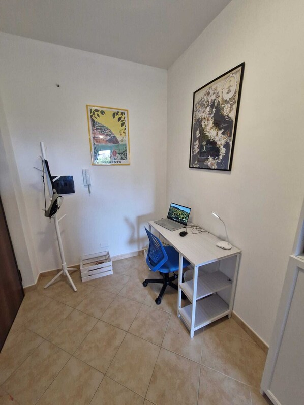 A small office space with a desk, chair, and a computer. There are two framed pictures on the wall, a whiteboard, and a small white cabinet.