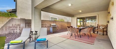 Un patio exterior con una parrilla, zona de estar y vistas de la casa.