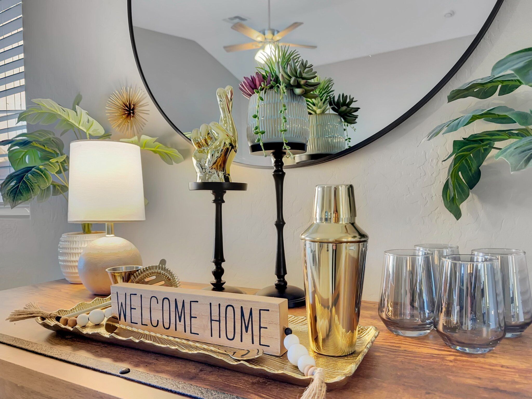 Interieurdecoratie met een 'WELCOME HOME' bord, een lamp, een decoratieve vogelsculptuur, een vetplant en een fles op een houten ondergrond.