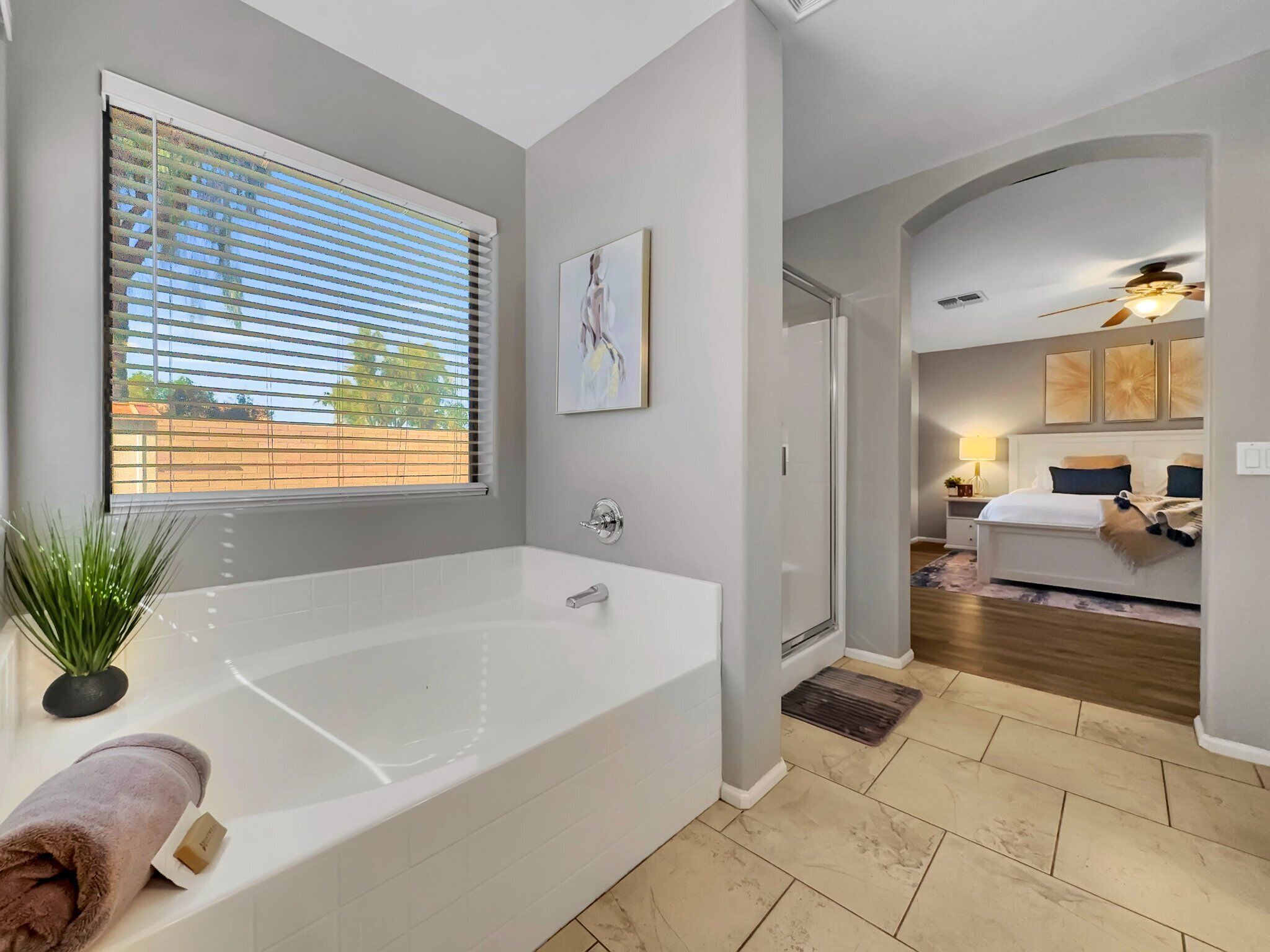 Une salle de bain moderne avec une grande baignoire, une fenêtre avec des stores, une plante en pot et une serviette posée sur le côté.