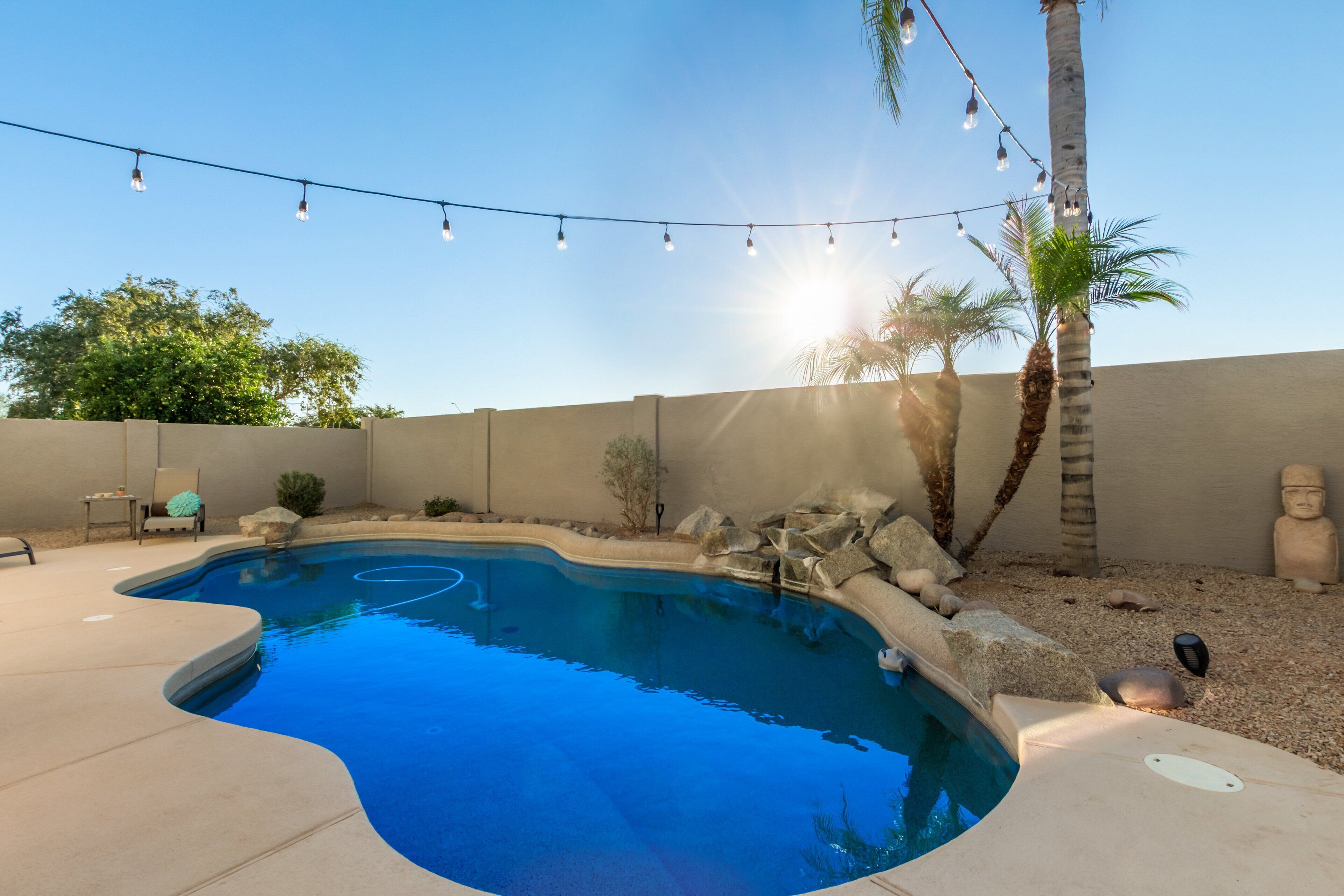 Una piscina de borde curvo, rodeada por un deck de concreto, palmeras y luces colgantes.