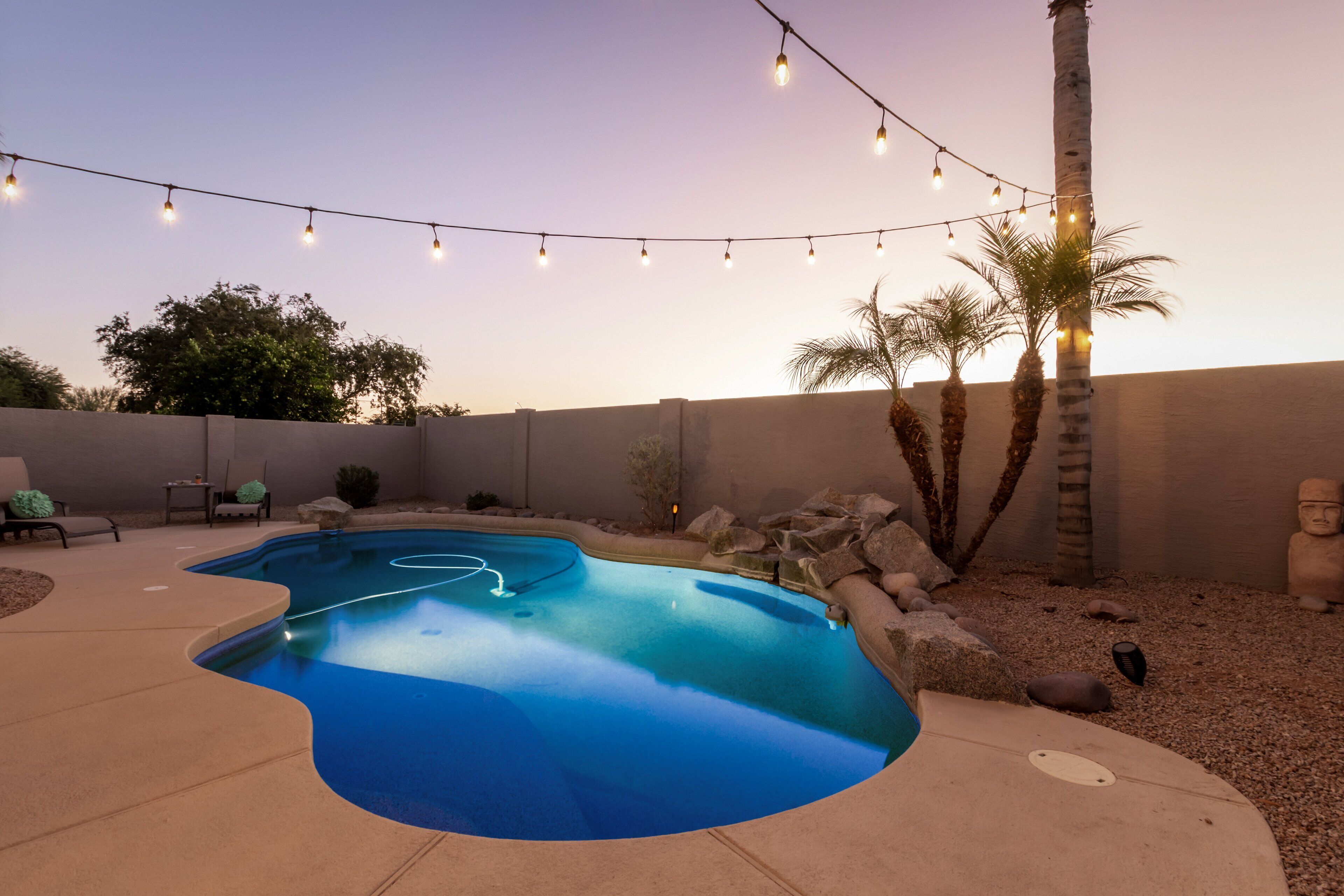 A swimming pool with a curved edge, surrounded by a patio area with chairs and a string of lights.