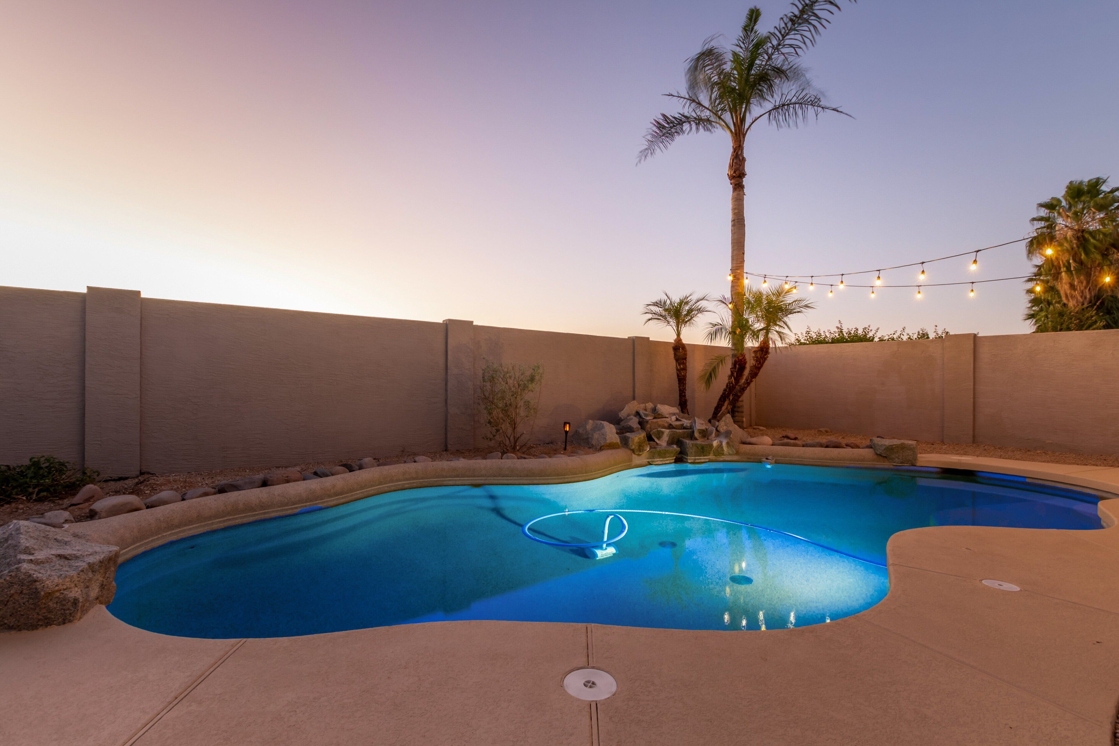 A swimming pool with a curved design, surrounded by a concrete deck and a low stone wall.