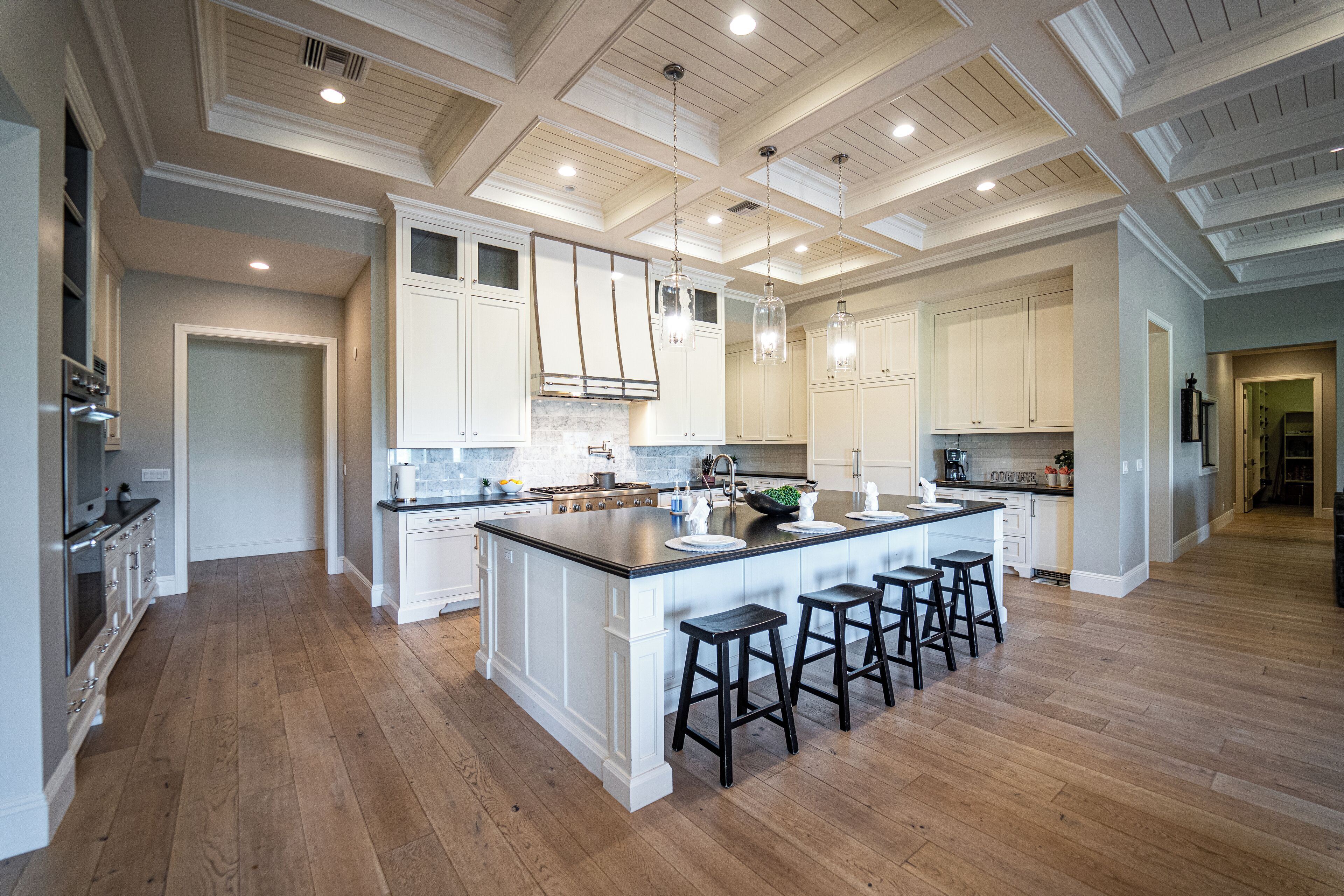 A spacious kitchen with a large island, white cabinetry, and wooden flooring.