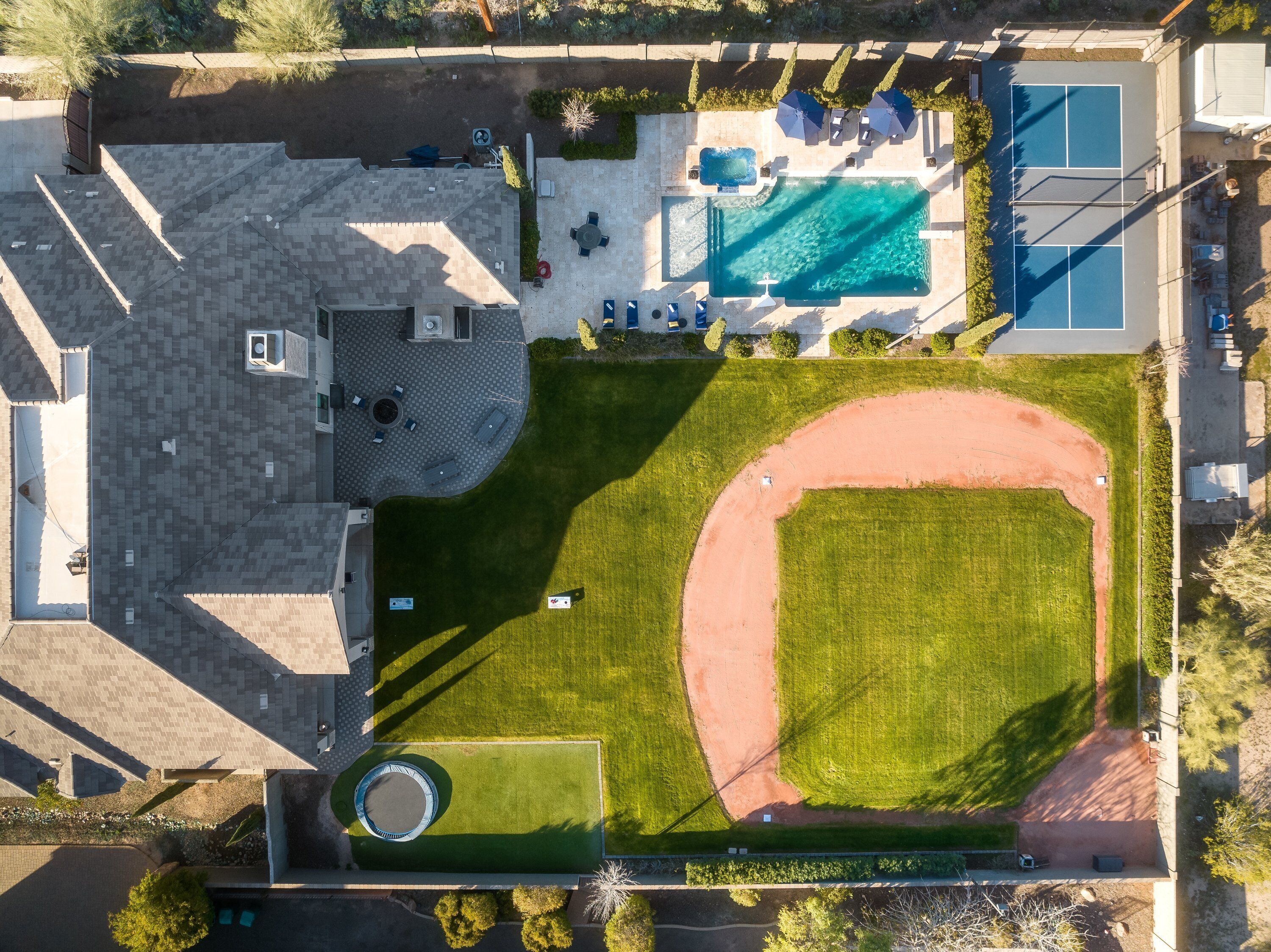 Vue aérienne d’une propriété dotée d’une piscine, d’un court de tennis et d’un jardin aménagé.