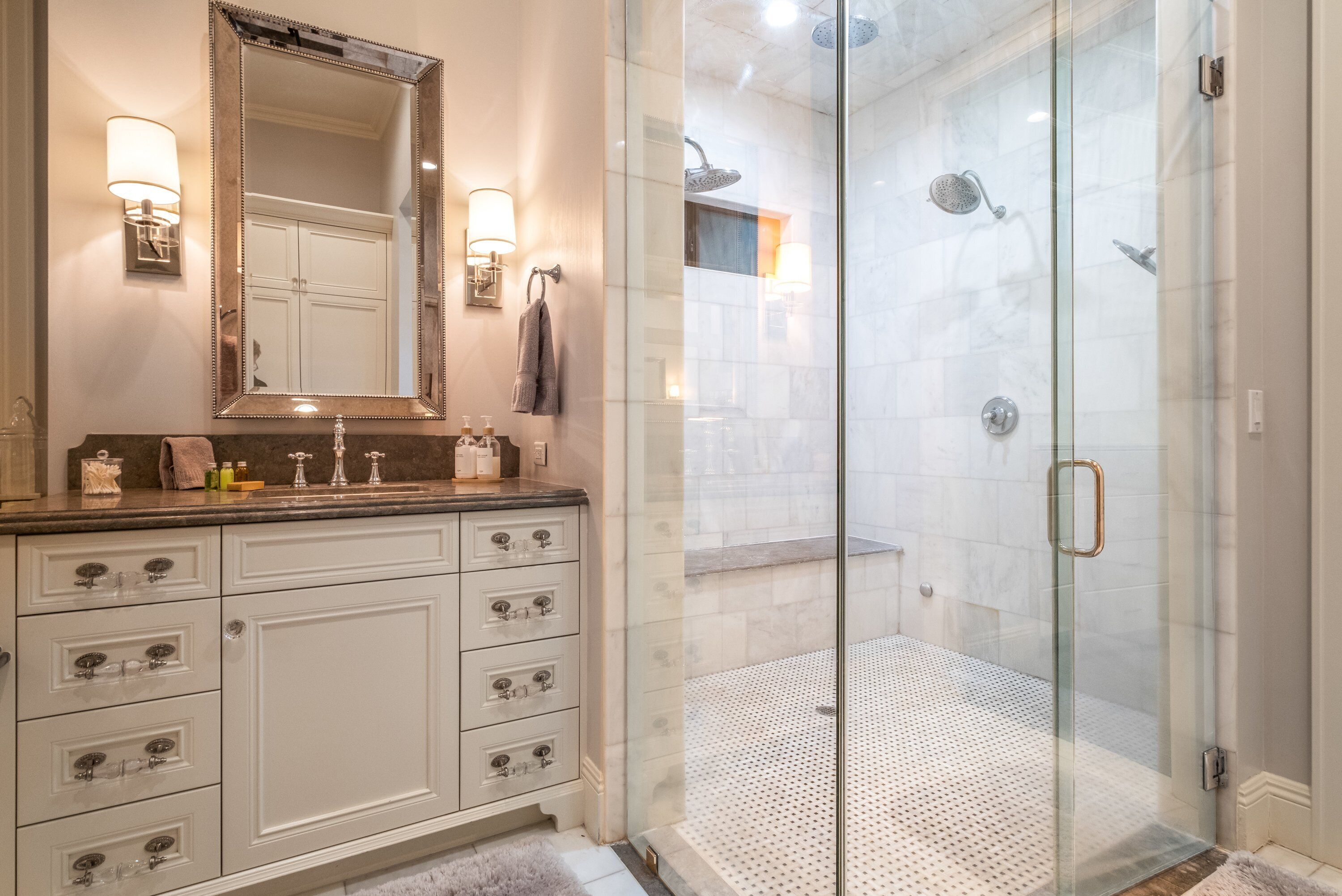 A bathroom with a glass-enclosed shower, a large mirror, and a marble countertop.