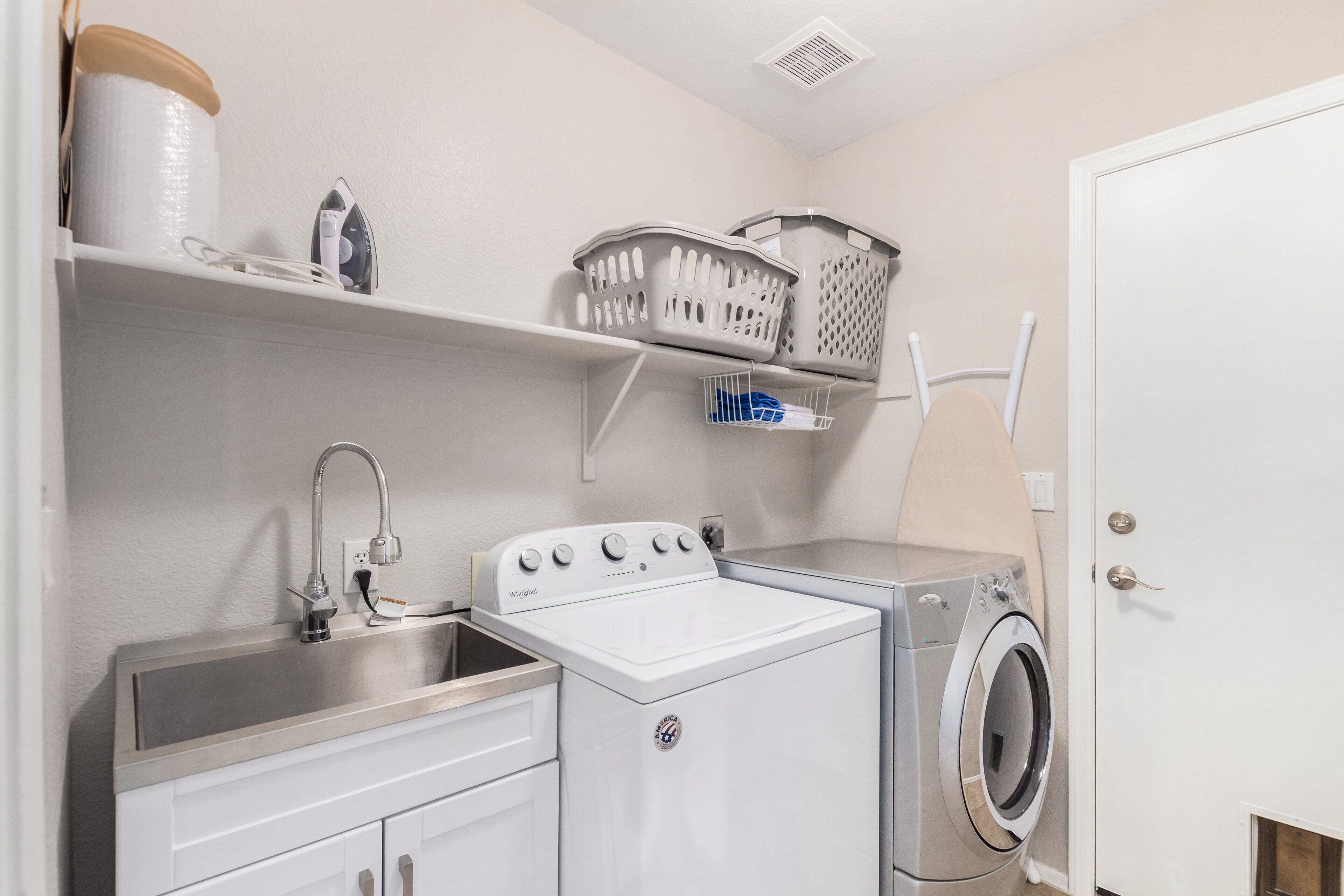 A compact laundry room with a washing machine, dryer, and a sink.