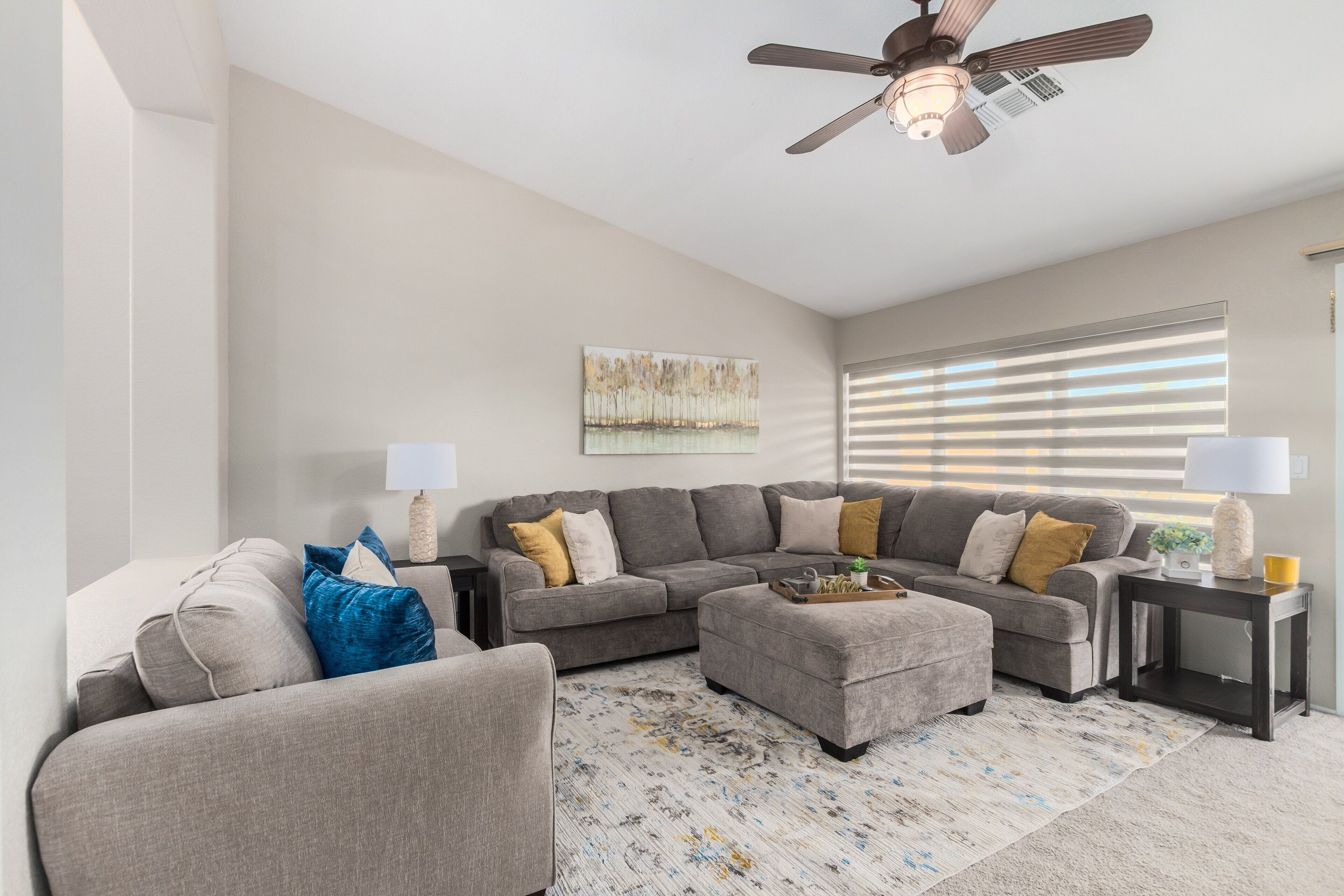 Ein Wohnzimmer mit einem Ecksofa, einem Hocker und einem Deckenventilator.