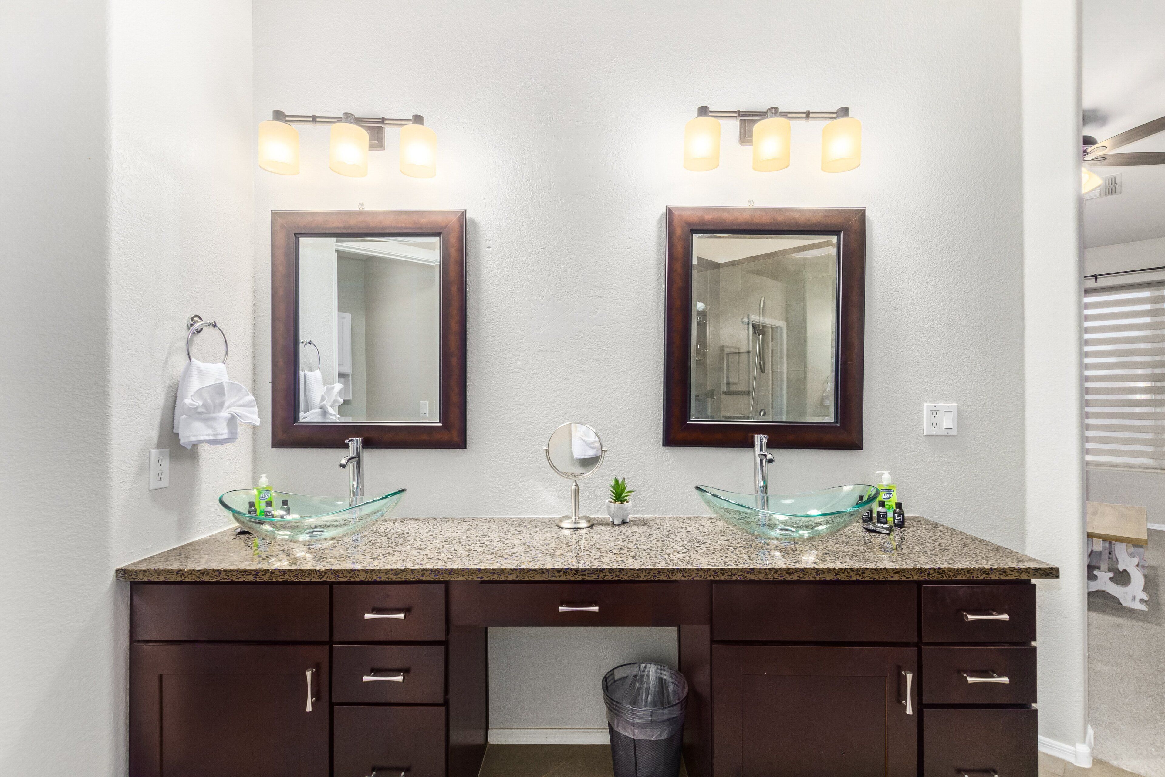 A bathroom with two sinks, each with a glass bowl, above a dark wooden vanity with drawers and a trash can.