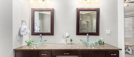 A bathroom with two sinks, each with a glass bowl, above a dark wooden vanity with drawers and a trash can.