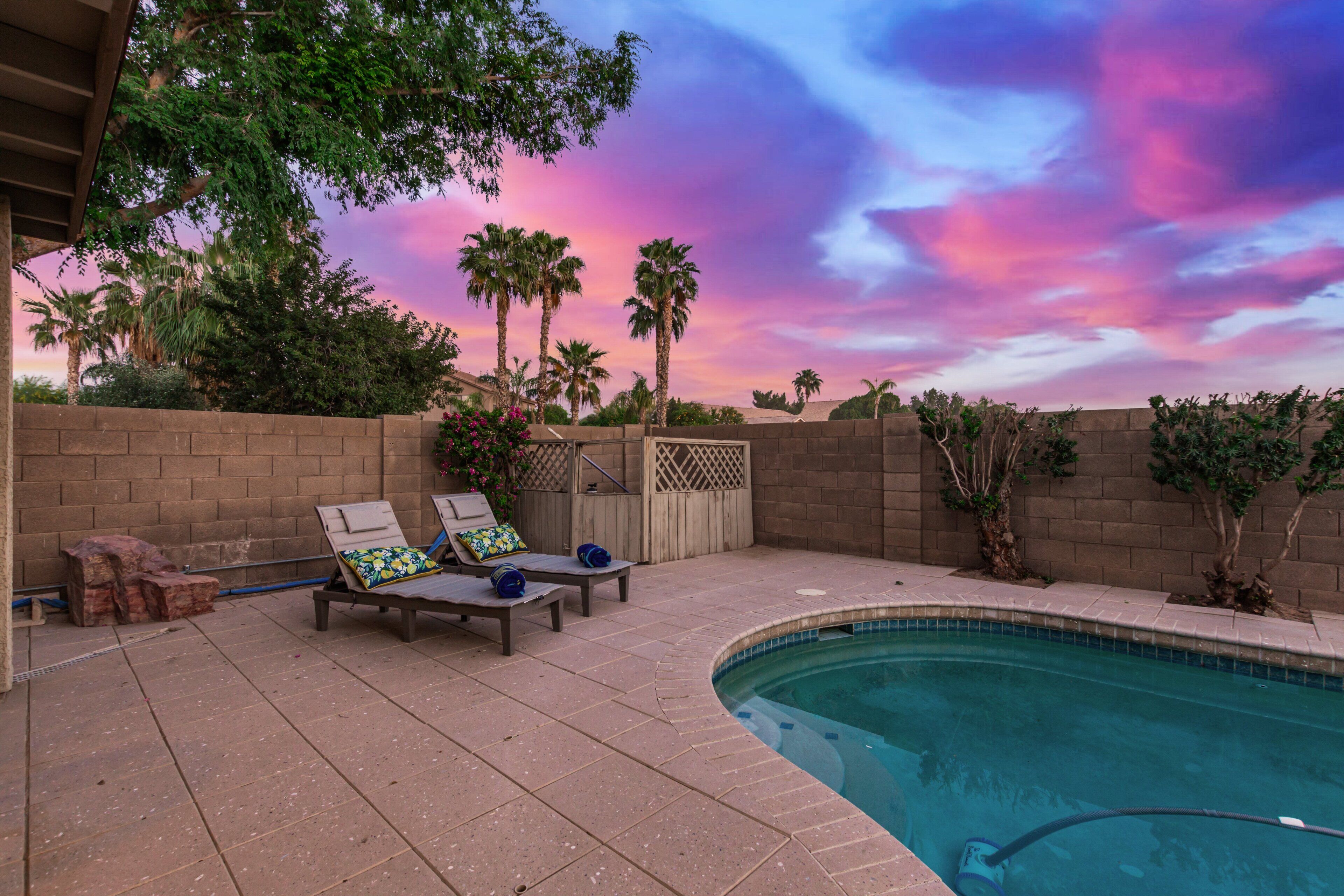 A backyard with a pool, two lounge chairs, and a wooden fence.
