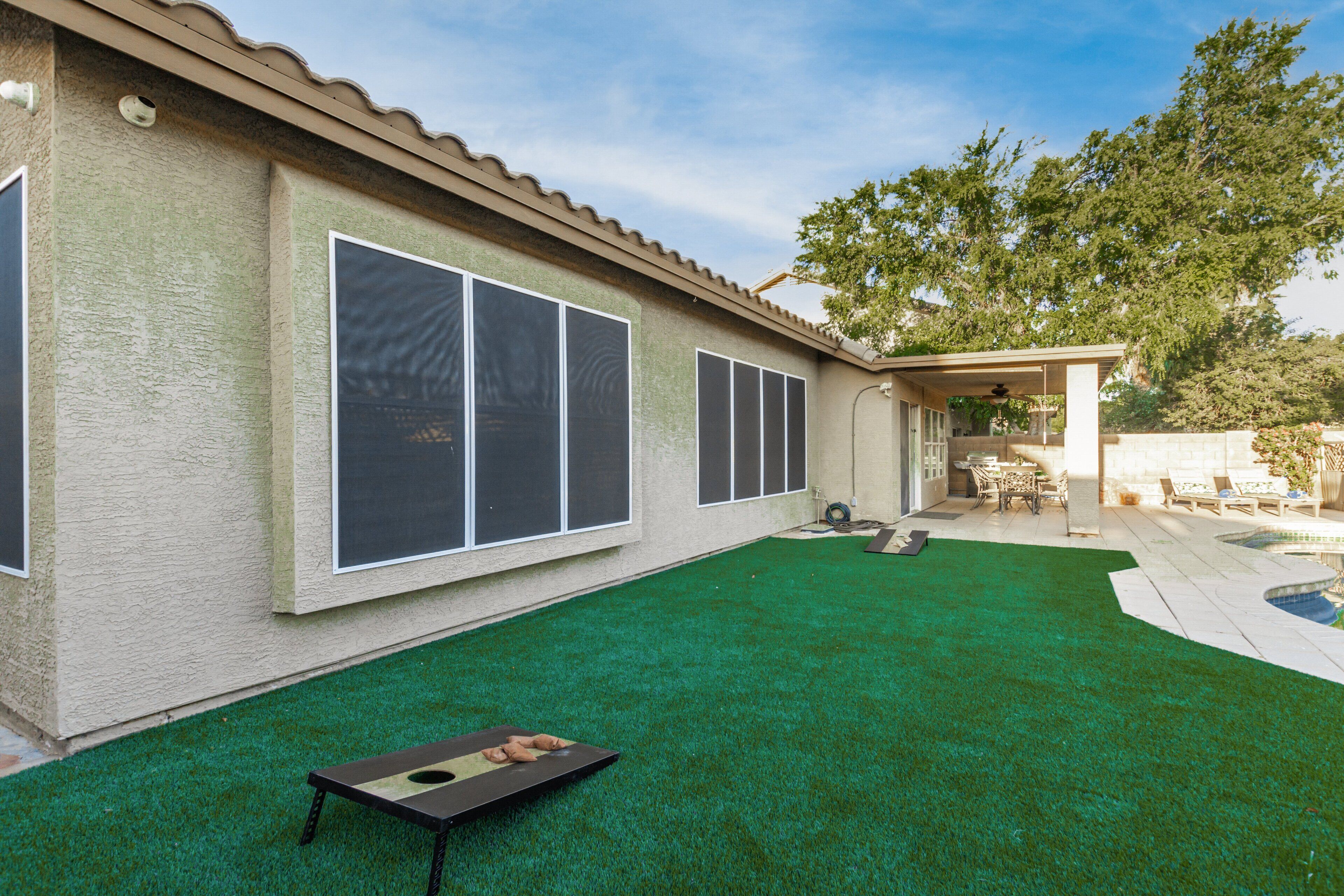 A backyard with artificial green turf, a pool, and a covered patio area.