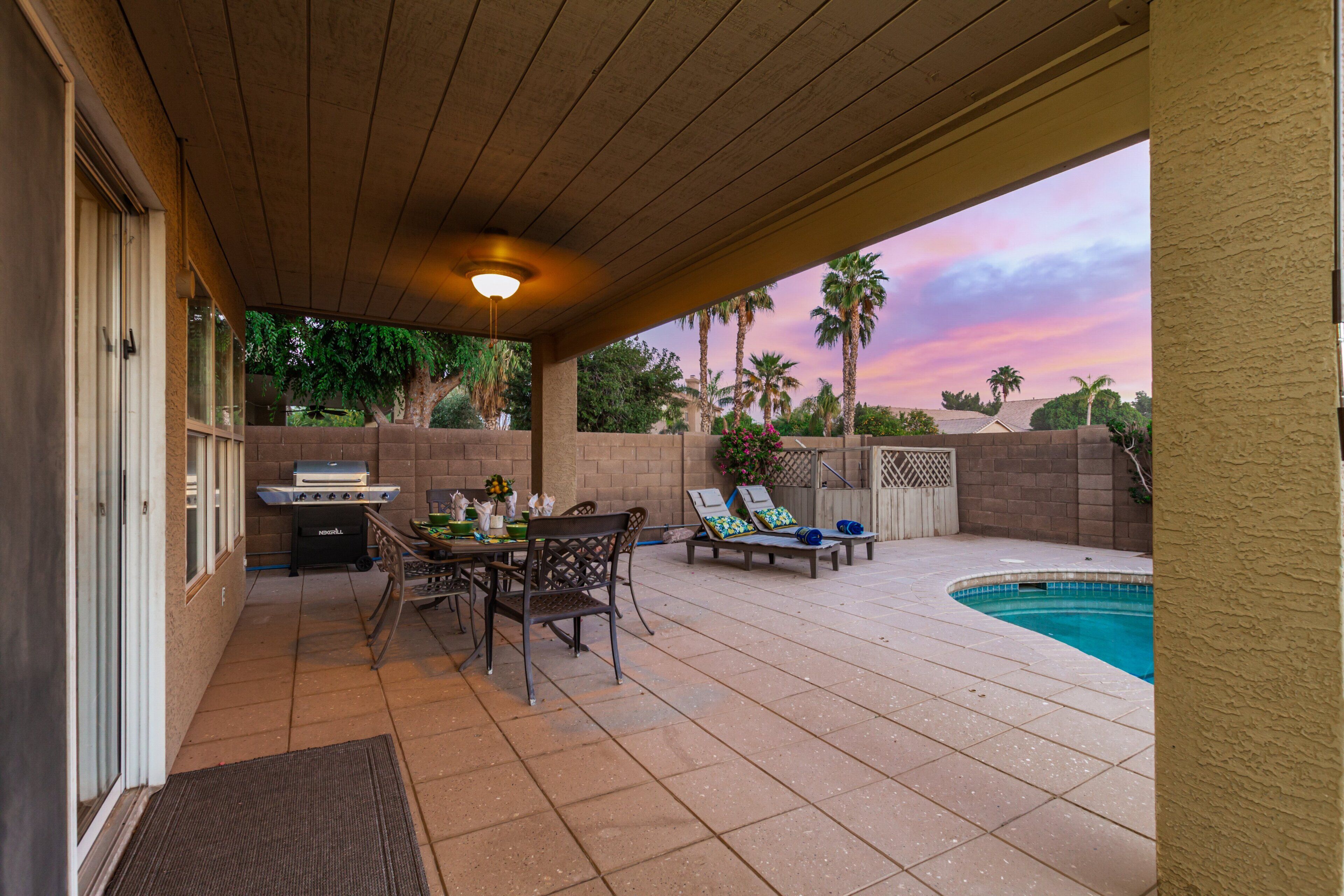 An outdoor patio with a pool, a grill, and lounge chairs.