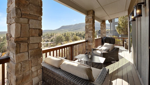 A covered outdoor deck with stone pillars, wicker furniture, and a view of mountains.