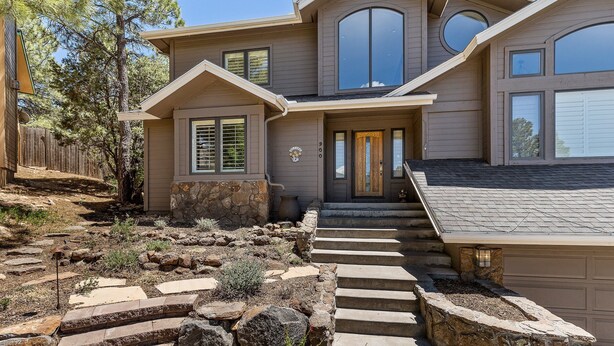 A two-story house with a stone staircase leading to the front door, surrounded by a landscaped garden with rocks and plants. - Sinagua Heights Flagstaff (Flagstaff)