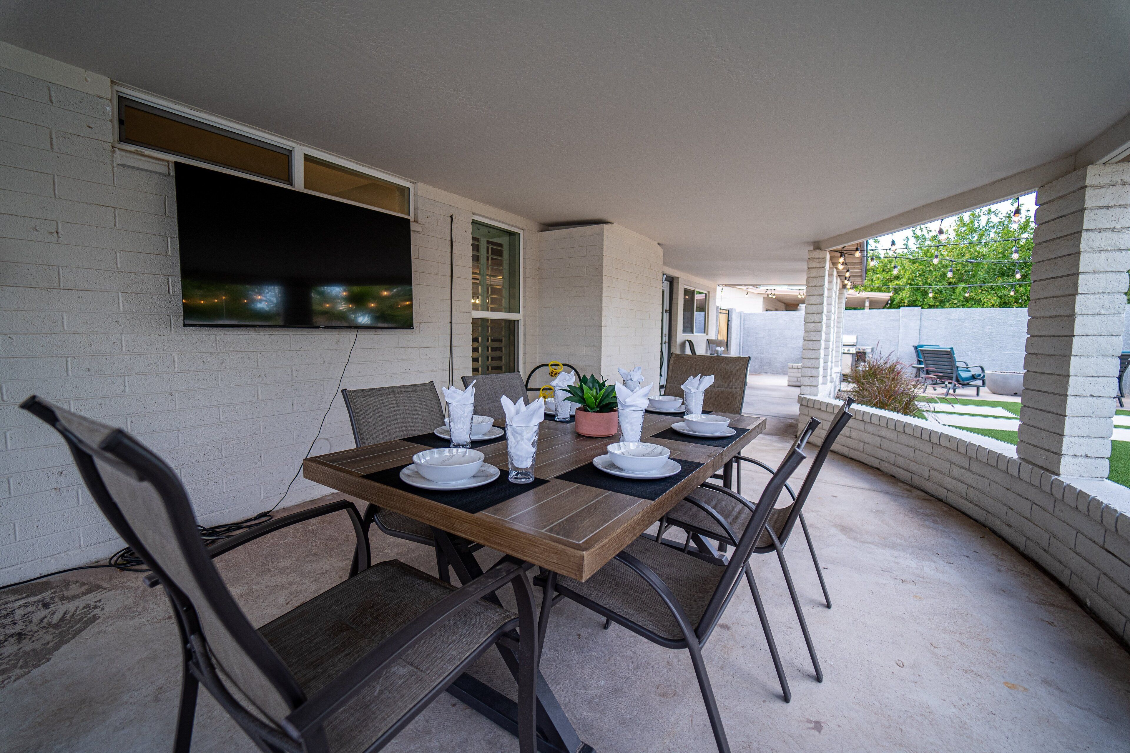A dining area with a table set for four, surrounded by chairs, a television mounted on the wall, and a potted plant.