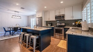 Una cocina moderna con armarios blancos, electrodomésticos de acero inoxidable y una isla central con taburetes de bar.