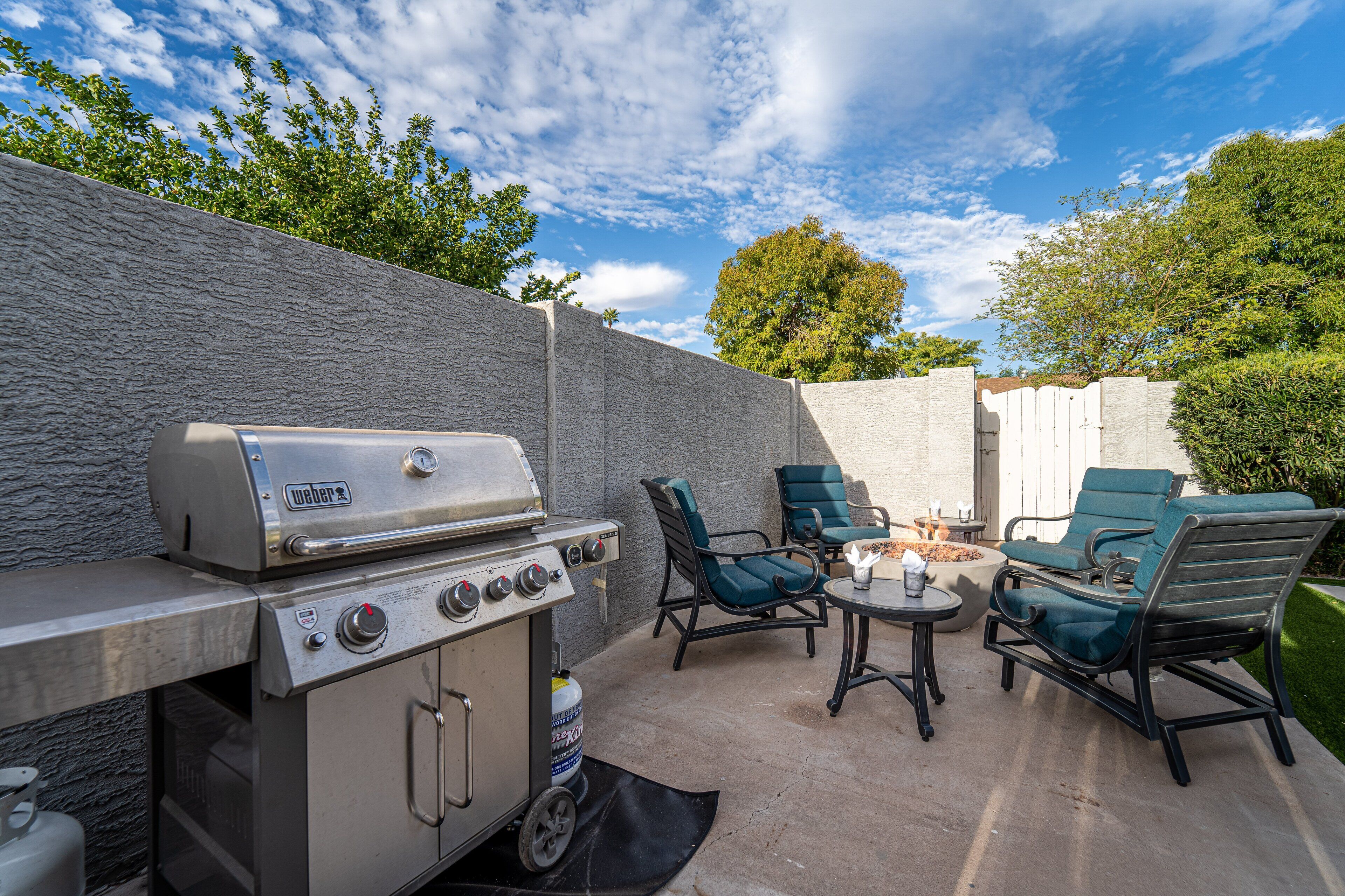 An outdoor patio with a grill, two chairs, and a small table.
