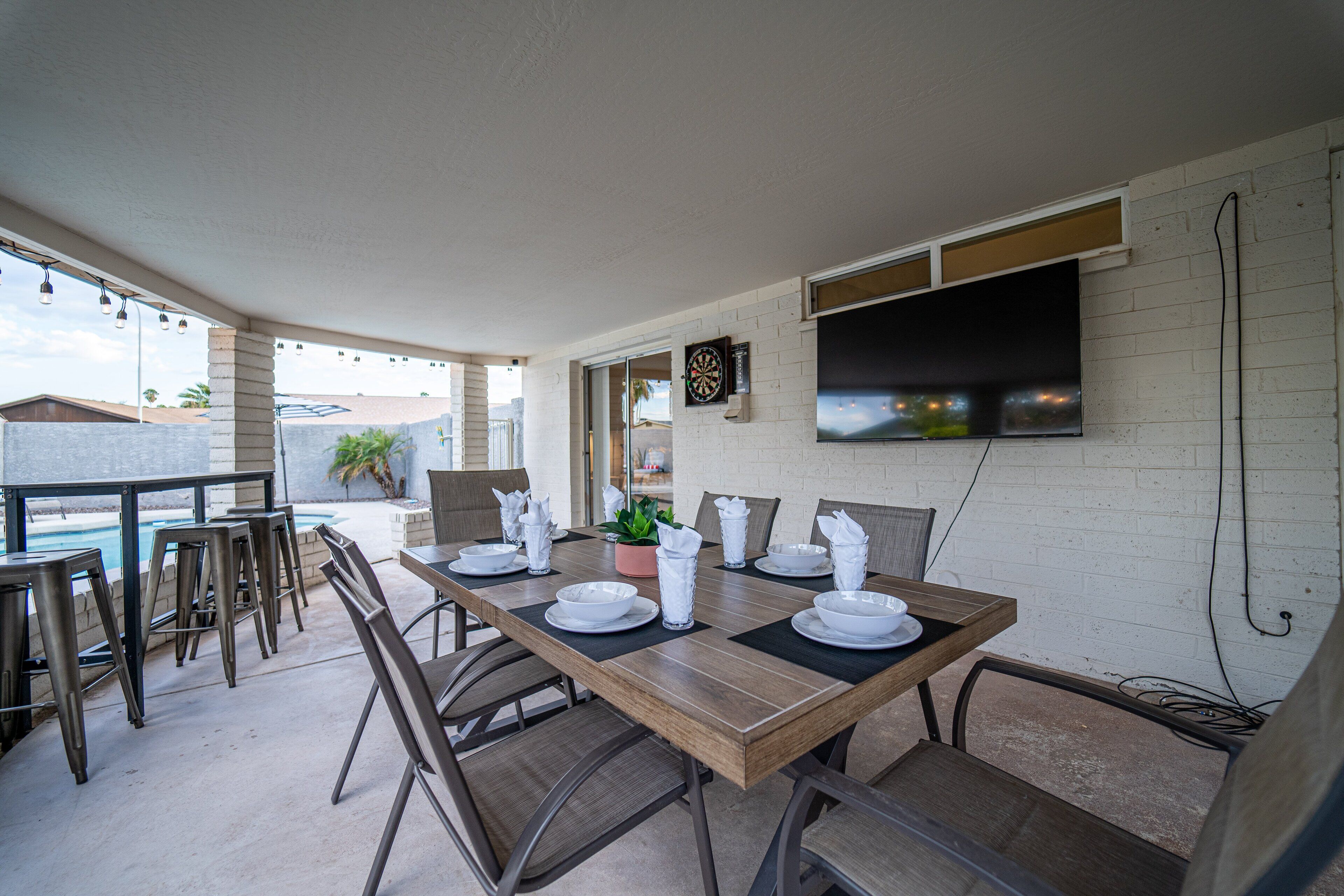 A dining area with a pool view, a flat-screen TV mounted on the wall, and a casual seating arrangement.
