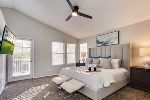 A bedroom with a large bed, a ceiling fan, a TV, and a window with blinds. - 73rd Glendale (Glendale)