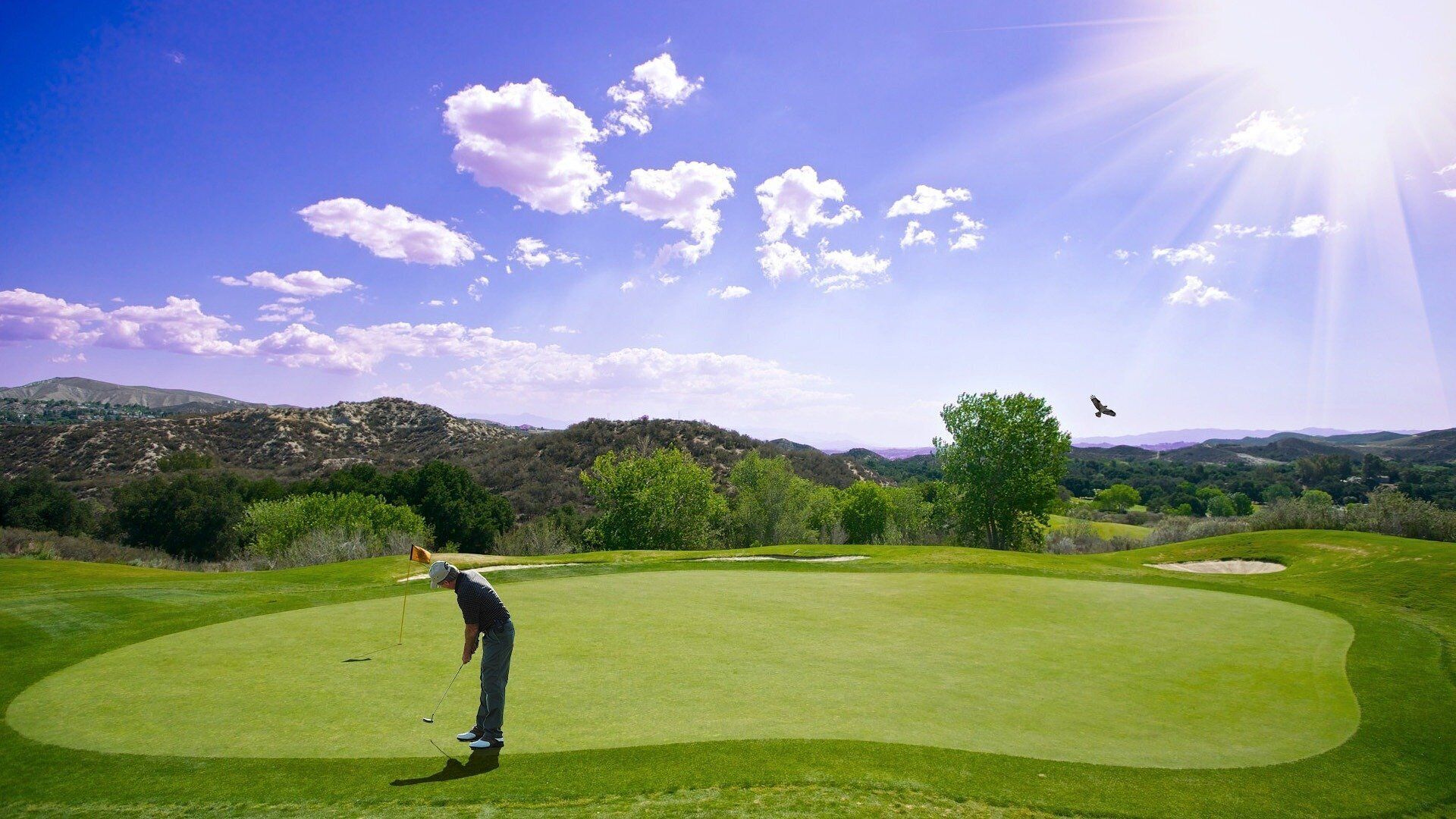 Un terrain de golf sous un ciel dégagé, avec des collines à l’horizon et un golfeur en plein élan.