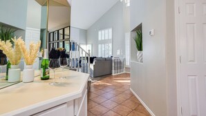 A modern kitchen with a white countertop, a dining area with a grey sofa, and a staircase leading to another level. - 73rd Glendale (Glendale)