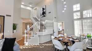 A spacious living area with a staircase, dining table set for four, and a large window providing natural light. - 73rd Glendale (Glendale)