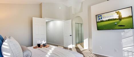 A bedroom with a bed, pillows, a TV on the wall, and a door leading to another room.