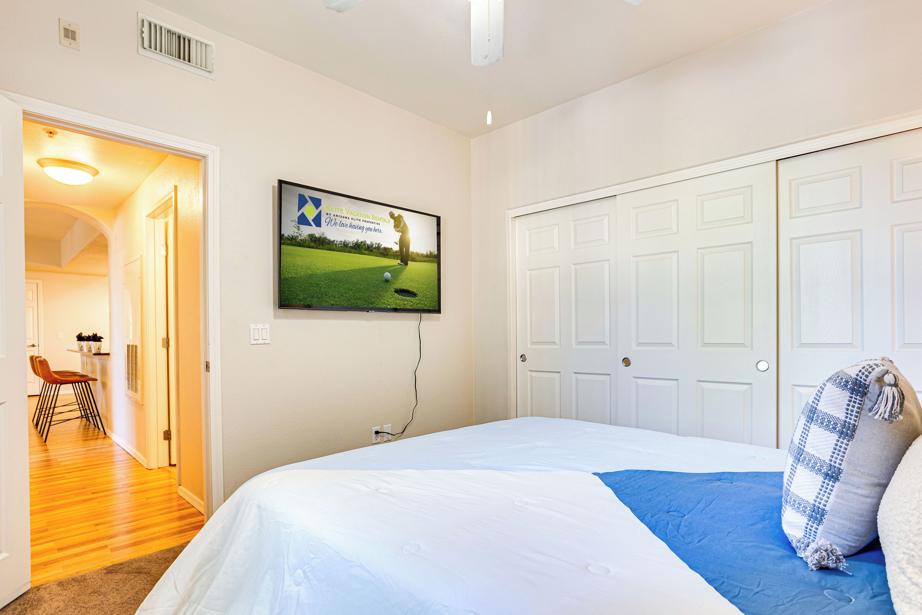 Un dormitorio con una cama grande, un televisor montado en la pared, un armario y una puerta que da a otra habitación.