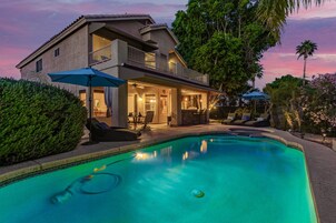 Una casa de dos pisos con piscina, mobiliario exterior y un balcón.