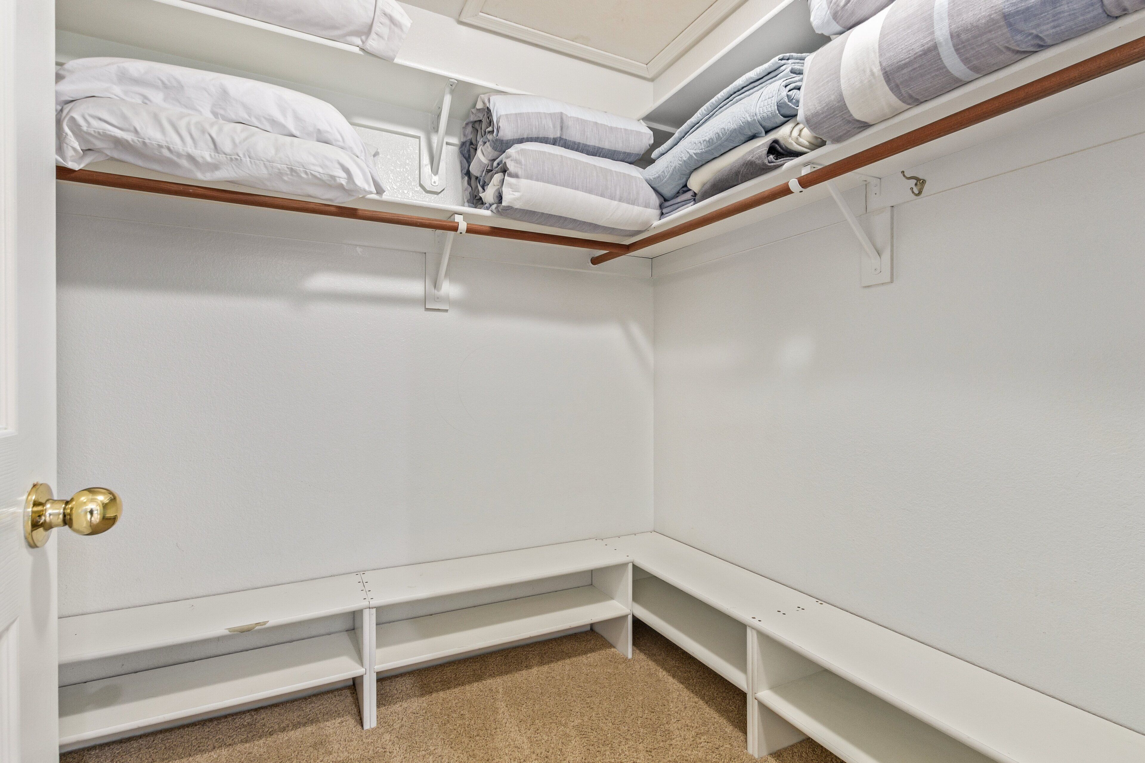 A corner closet with white walls, a wooden bench, and shelves for folded clothes.