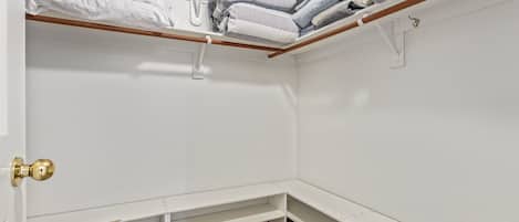 A corner closet with white walls, a wooden bench, and shelves for folded clothes.