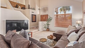Amplia sala de estar con un sofá modular grande, un televisor de pantalla plana, una escalera y un ventanal con persianas.